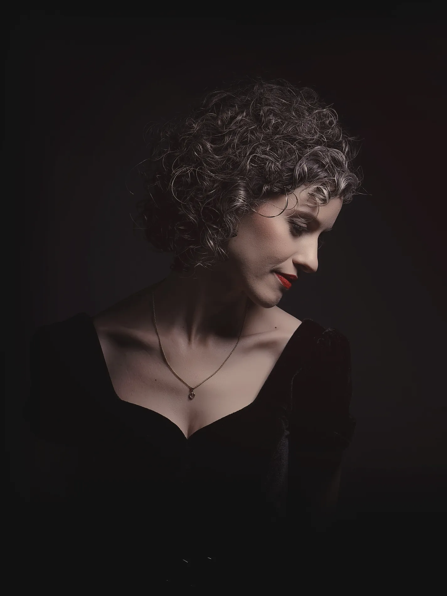 Alicia Sevilla de perfil, vestida de negro sobre fondo oscuro